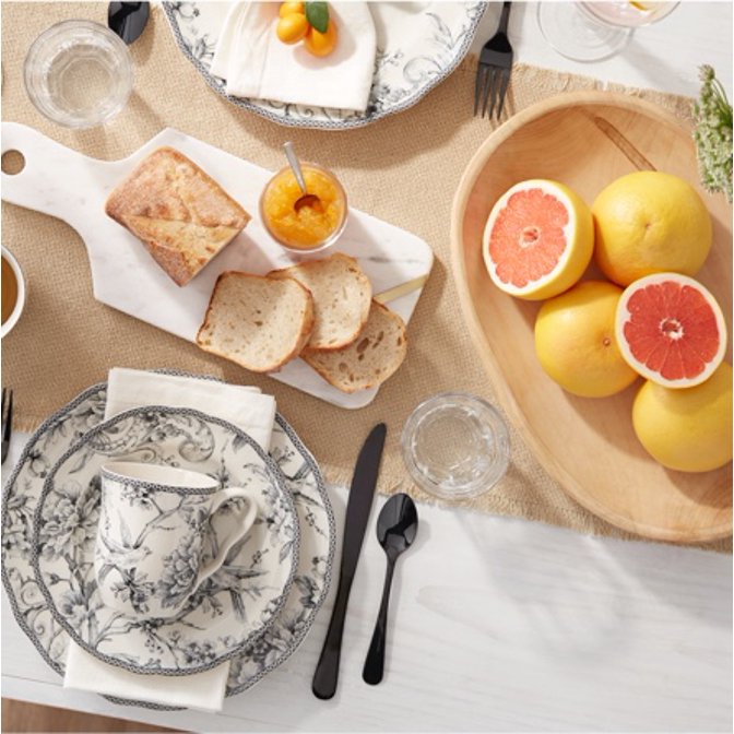 A spring table setting with floral dinnerware, a marble cheese platter, and a bowl of grapefruit.