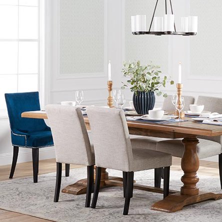 A transitional style dining room with blue velvet end chairs, a wooden traditional trestle table, and a traditional style chandelier.