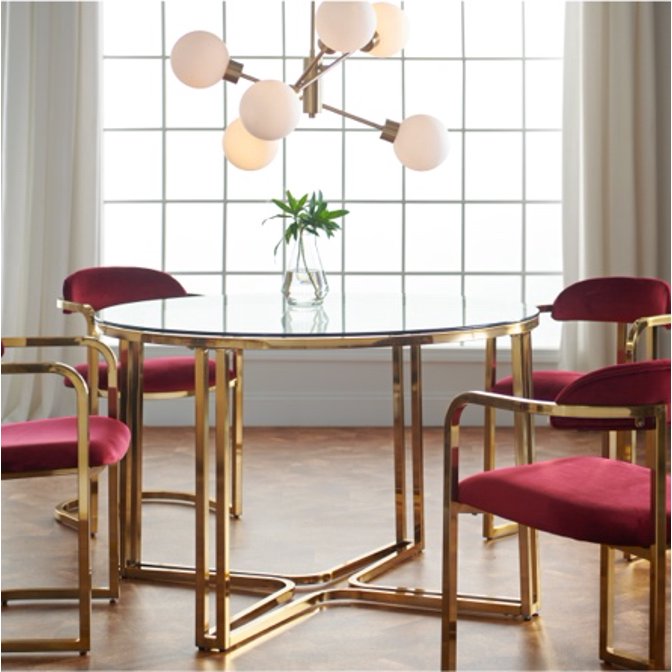 A Retro Glam dining room with gold framed chairs and pink velvet cushions as well as a gold sputnik chandelier above the round gold and marble dining room table