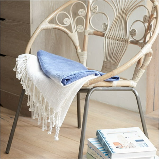 A woven bamboo accent chair accented with a blue ombre throw blanket is next to a dresser with wellness decor. It's all styled to be a meditation nook in a boho minimalist bedroom