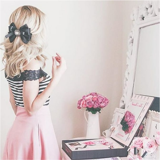 Lexie of Jadore Lexie Couture looking at her glam style vanity in her glam style home with a baroque style decorative mirror in white and a jewelry box on the counter