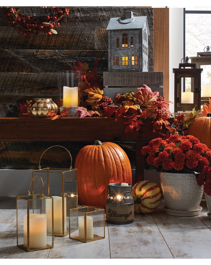 An entryway bench decorated with a galvanized metal lantern shaped like a house, lots of fall foliage, a pumpkin and candles.