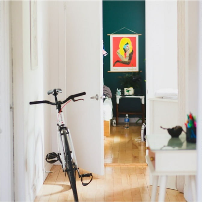An image of an entryway with a bicycle and a bright 80s inspired painting on dark teal walls
