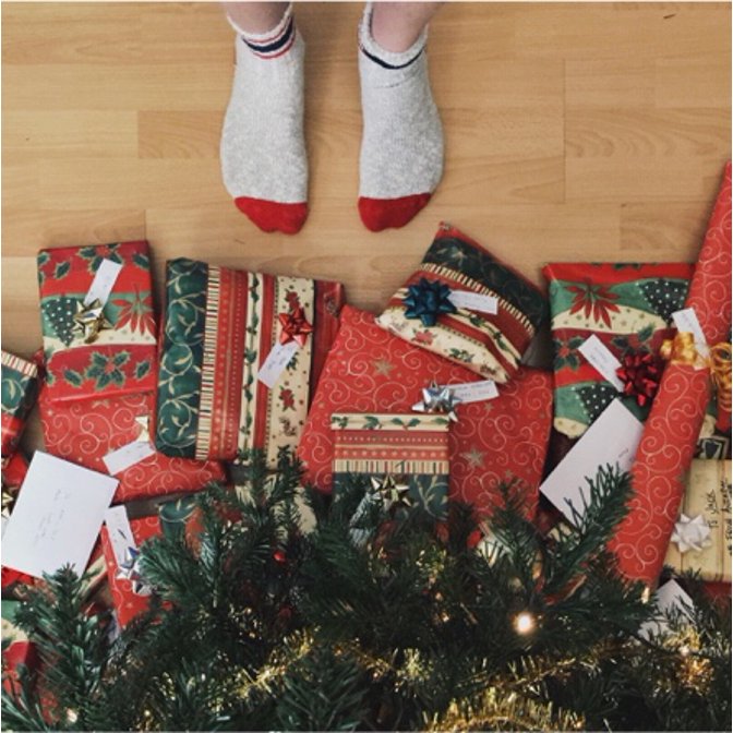A picture of someone at the foot of a Christmas tree staring down at a pile of Christmas presents