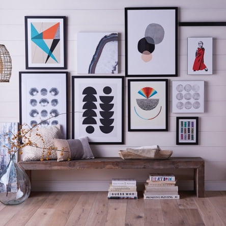 A modern gallery wall with a portrait of Twiggy and abstract prints above a rustic entryway bench. Introduces a blog post about how to style a unique gallery wall.