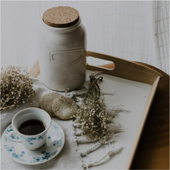 A hygge vignette of a rustic wooden tray with a ceramic candle, pine needles and a cup of tea in a porcelain cup with saucer.