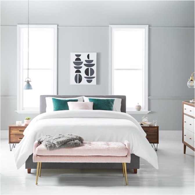 A modern bedroom with mid-century style furniture and glam accents including a pink velvet bench with gold legs, a walnut credenza and velvet throw pillows.