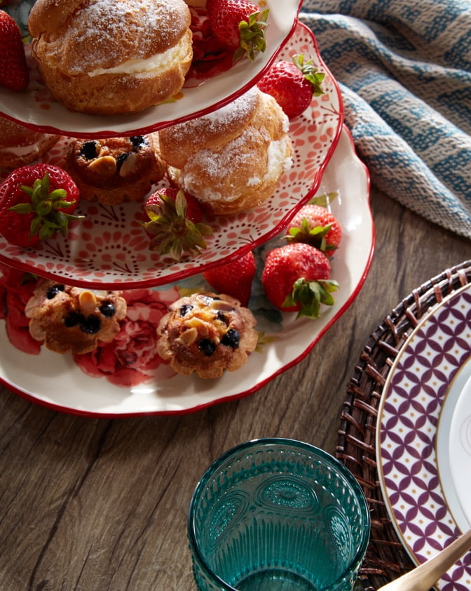 A close-up shot of a three-tiered serving tray with cream puff pastries, strawberries and other desserts on a rustic table with a kitchen napkin for spring brunch.