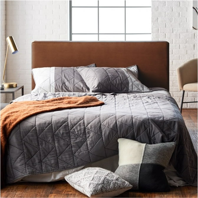 A refined industrial bedroom with a camel colored headboard, gray bedding, and a warm wooden nightstand.