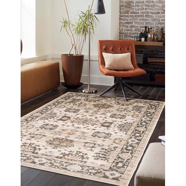 ECARPET Gloria traditional area rug featuring beige background with detailed floral and geometric motifs in brown and blue hues on dark hardwood floor next to leather chair, potted plant, and shelving unit.