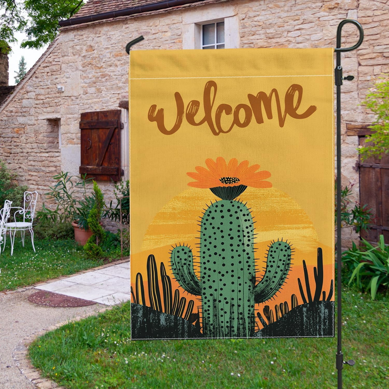 A backyard scene featuring a cactus-themed garden flag with a hippie western aesthetic, surrounded by desert landscaping.