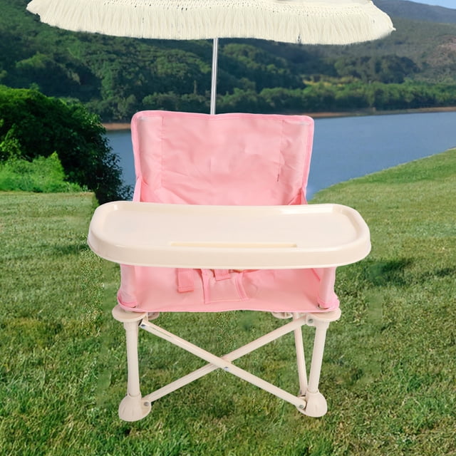silla de playa portátil para bebé Anggrek rosa con bandeja desmontable, vista frontal centrada; silla plegable en tela Oxford rosa sobre marco en X de acero con acabado crema, bandeja plástica crema de aprox. 40 x 17 cm colocada, arnés visible y patas compactas, fondo de césped y sombrilla. Adecuada para alimentar a niños pequeños; su tamaño compacto la hace adecuada para viajes y almacenamiento en la bolsa incluida.