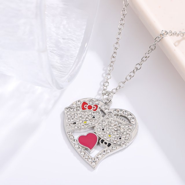 collar con forma de corazón de niña con un lindo gato kt, colgante de llave con diamantes de imitación de hello kitty súper lindo japonés, collar de aleación con un gato japonés. Vista frontal centrada de un collar de aleación plateada con cadena de eslabones y colgante en forma de corazón; el colgante tiene dos caras de gato decoradas con diamantes de imitación, un lazo rojo esmaltado en la parte superior y un pequeño corazón rosa esmaltado en la base. Fondo blanco minimalista; también es adecuado como regalo juvenil.