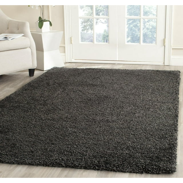 Safavieh Milan Harlow dark gray solid shag area rug displayed in a modern living room setting with light wood flooring and natural light from glass doors.