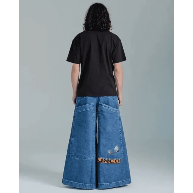 jnco-pantalones vaqueros holgados para hombre y mujer, pantalón ancho de cintura alta, harajuku, hip hop, retro, bordado con gráfico de calavera — vista posterior de pie con camiseta negra mostrando denim azul medio hasta el tobillo, corte de pierna ancha y cintura alta, costuras y grandes bolsillos traseros, bordado de calavera y etiqueta textil naranja en la pernera derecha, cierre de cremallera y botón; adecuado para looks harajuku o hip hop y como pieza llamativa de estilo retro.