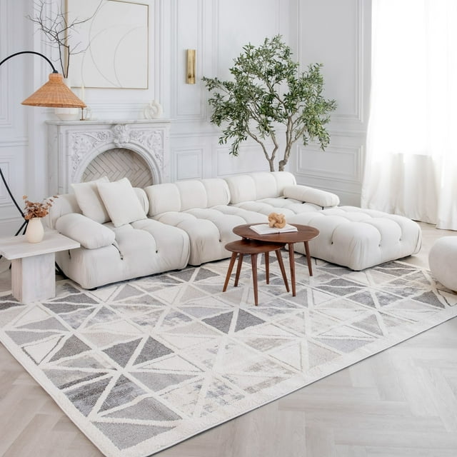 Cream grey Nimbus geometric indoor area rug in modern living room setting with white tufted sectional sofa, wooden nesting tables, and decorative fireplace.