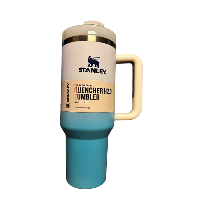 termo stanley quencher h2.0 flowstate tumbler multicolor, vista frontal centrada de vaso térmico alto con asa rectangular; base turquesa mate, banda central beige con etiqueta y logo Stanley, tapa crema con borde metálico y boquilla de flujo; fondo blanco neutro, a menudo usado para mantener bebidas accesibles durante viajes.