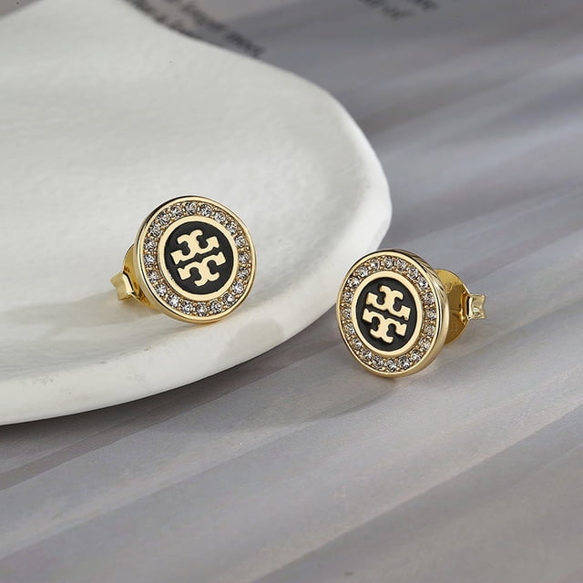 pendientes de plata clásica tory burch doble t joyería chapado en oro de 18 quilates redondos tb para damas aretes redondos con logo TB central sobre disco negro y aro exterior de cristales, vista frontal cercana sobre base clara y fondo gris. Su tamaño compacto los hace adecuados también como aretes de uso diario.