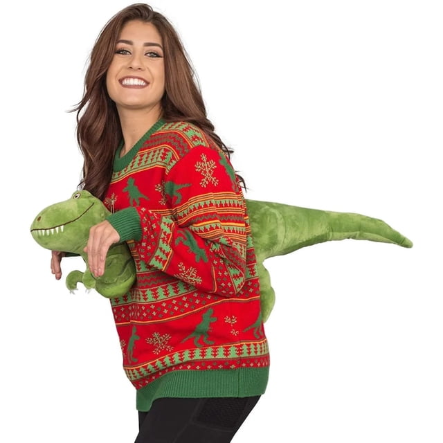 3d nuevo en suéter navideño feo para hombres y mujeres moda high street vintage manga larga pareja jersey prendas de punto tops divertidos suéter rojo con dinosaurios verdes 3D, vista 3/4 lateral con modelo sujetando peluche Tyrannosaurus Rex; cuello redondo, puños y borde inferior verdes, patrón de copos y motivos geométricos en tejido de punto.