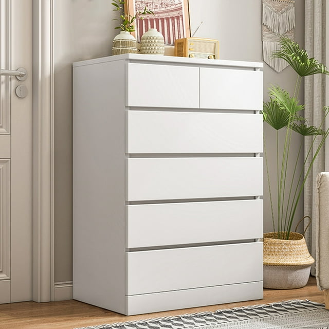 Commode, Commode Haute Blanche avec 6 Tiroirs en Bois, Comprenant 4 Grands Tiroirs et 2 Tiroirs Plus Petits pour un Rangement Organisé. Fabriquée en Bois durable de Type Assiette, Cette Commode de Chambre Gain de Place Mesure 23,6 Pouces de long, 16,1 Pouces de large et 42,9 Pouces de Hauteur. Positionnée dans un Cadre de Chambre Lumineux avec des accents Décoratifs sur le Dessus, Idéale pour le Mobilier de Chambre Moderne.