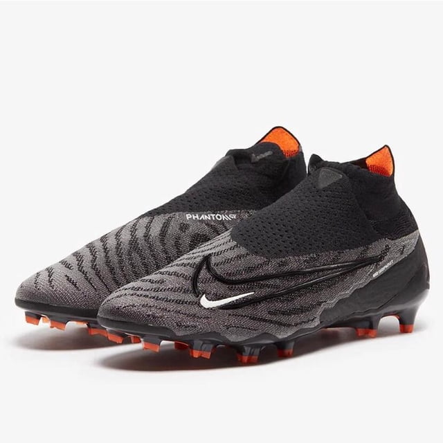 phantom gx elite fg botas de fútbol de nuevo estilo suela original impermeable botines gris y negro con tejido de punto, suela FG con tachones naranjas, cuello elástico tipo calcetín y detalle de logo lateral; vista 3/4 frontal sobre fondo blanco, adecuados para césped natural y suelen usarse también en entrenamientos rápidos.