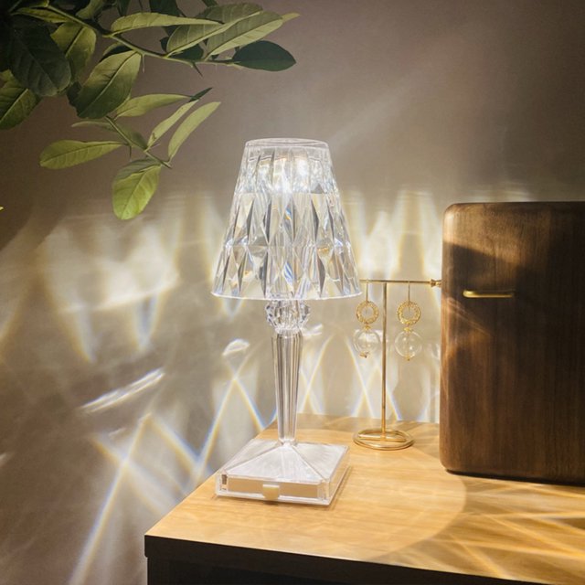 lámpara luz de mesa transparente s de escritorio de cristal acrílico decoración lámpara de mesa prisma transparente con pantalla facetada y base acrílica en vista 3/4 sobre buró de madera; luz blanca que proyecta patrones prismáticos en pared, cable de 150 cm y botón de interruptor visibles; ideal como iluminación decorativa para dormitorio y escritorio y adecuada para ambientar sesiones de lectura ligera.