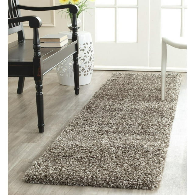 Safavieh Milan Harlow solid shag area rug in beige and brown tones on a light wood floor, styled with black wooden chair, white ceramic side table, and natural light from window.