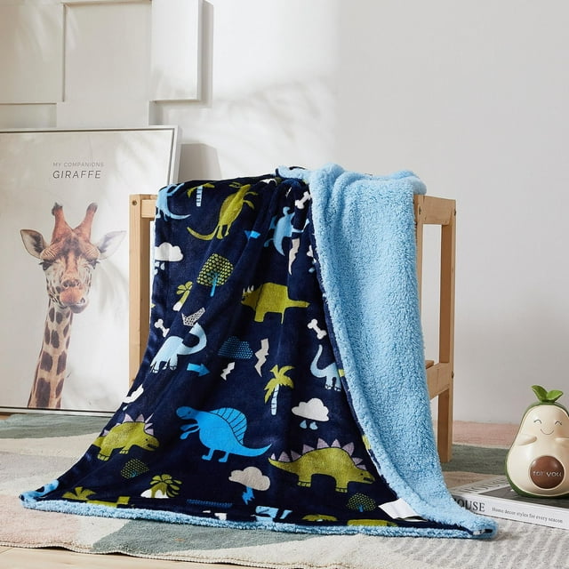 Soft reversible children's blanket featuring colorful dinosaur patterns on a navy base and plush light blue sherpa fleece, displayed over a wooden chair in a cozy room setting.