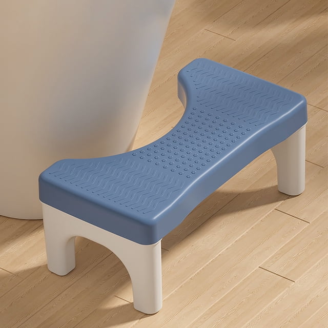 taburete de baño en cuclillas para adultos y niños | reposapiés ergonómico con ángulo de 35° para aliviar el estreñimiento | orinal antideslizante con superficie acolchada | compatible con inodoros Azul Tingxian, vista 3/4 frontal de un reposapiés compacto con superficie acolchada texturizada y patrón de ondas y puntos; borde curvo con recorte para encajar frente al inodoro, cuatro patas blancas con bases antideslizantes y acabado mate, colocado sobre piso de madera junto a un inodoro. También suele usarse como soporte de postura para niños durante el entrenamiento.