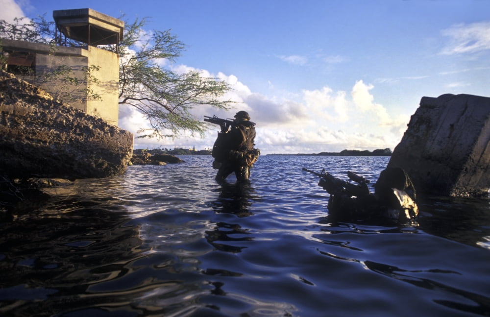 Two Navy SEALs transition from under the water and begin crossing the beach wearing Draeger LAR