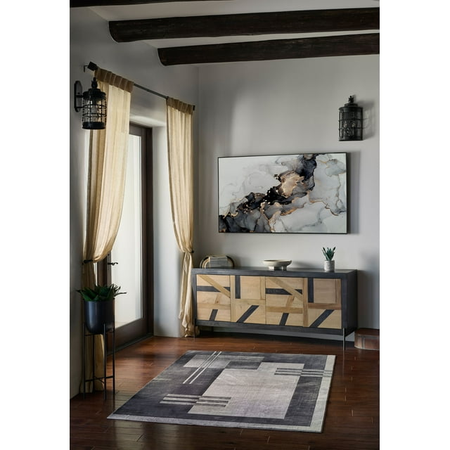 ECARPET Sorelle contemporary area rug featuring a geometric design in gray and beige tones, placed on hardwood flooring beneath a wooden sideboard with abstract wall art above, illuminated by natural light from nearby windows.
