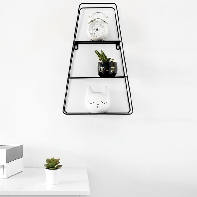 Truu Design Decorative Trapezoid Floating Wall Shelf with black metal frame and three tiers, mounted on a white wall, displaying a white alarm clock, a black cat-shaped planter with a succulent, and a white cat-shaped ceramic decor piece, suitable for showcasing small decorative items in living rooms or offices.