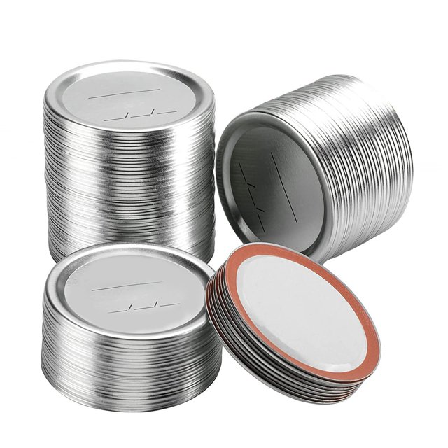98 Count 70mm Regular Mouth Canning Lids for Ball and Kerr Canning Lids, shown in stacks and a spread-out arrangement. These split-type metal mason jar lids are silver in color and made of tinplate with a silicone ring for airtight sealing. Suitable for preserving food, jams, grains, and beverages, they are rust-proof, reusable, and compatible with refrigerators, dishwashers, and microwaves. The lids feature a writable surface for marking dates or food-related information.