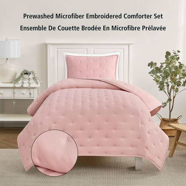 Twin size pink blush prewashed microfiber comforter and matching pillow sham with subtle embroidery on a white bed frame in a modern bedroom.