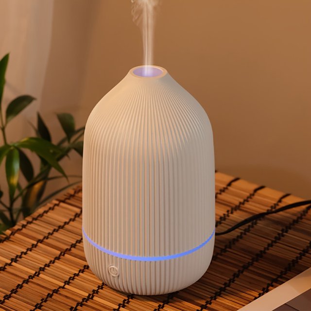difusor y humidificador de aceites esenciales 2-en-1, vista frontal cenital de un difusor portátil blanco acanalado con anillo de luz ambiental LED azul en la base y vapor saliendo por la parte superior; alimentado por USB, apagado automático, adecuado para ambientar graduaciones y celebraciones en casa.