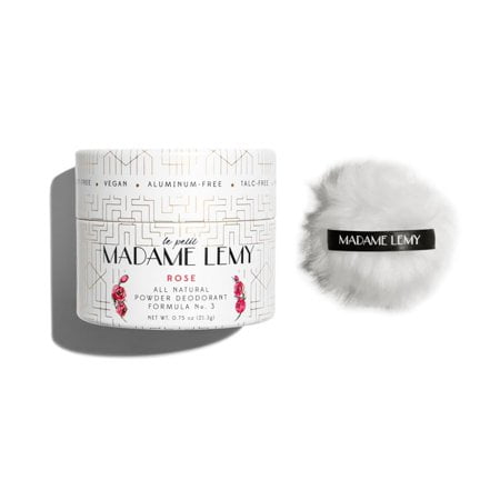 Madame Lemy Talc-Free Powder in Rose scent, a multi-purpose deodorant and body powder in a 0.75 oz container. The image features a white cylindrical container with gold geometric patterns and rose illustrations, paired with a fluffy white puff labeled 'Madame Lemy' on a black ribbon. This vegan, aluminum-free, and plastic-free product is ideal for travel-size body care, offering anti-chafing benefits and long-lasting odor protection.