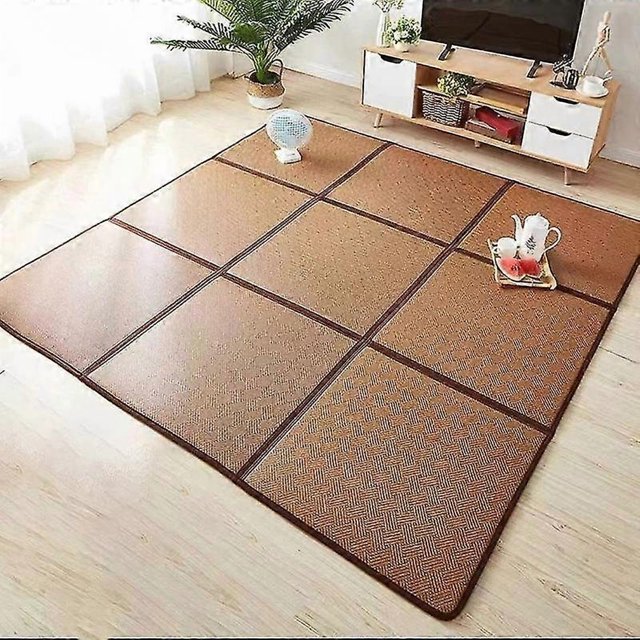 rattan mat summer japanese tatami rugs and carpets for home living room folding mat bedroom rug stitching rattan crawl carpet — vista 3/4 frontal de una alfombra tatami rattan de tono marrón claro formada por paneles cosidos con borde marrón oscuro y textura tejida visible; colocada sobre piso de madera frente a mueble de TV y planta, no lavable a mano ni a máquina, limpiar con paño o aspiradora. Ideal también como tapete plegable para sentarse o área de juego ligera.