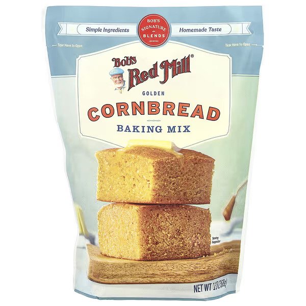 Bob's Red Mill Golden Cornbread Baking Mix, 13 oz (368 g) package. The front of the bag features an image of two golden cornbread slices stacked on a wooden surface, with the brand's logo and product name prominently displayed. The packaging highlights 'Simple Ingredients' and 'Homemade Taste' at the top.