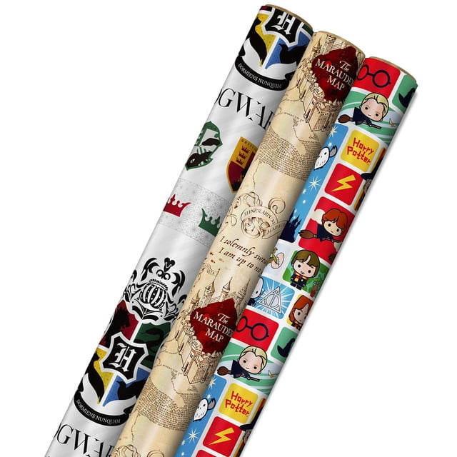 hallmark harry potter - papel de regalo con líneas cortadas en el reverso (3 unidades, 60 pies cuadrados, mapa de merodeador, escudo de hogwarts), para cumpleaños, gr paquete de tres rollos en vista 3/4: rollo con crestas de Hogwarts en blanco, rojo y azul; rollo con el Mapa del Merodeador en tono pergamino; rollo con ilustraciones tipo caricatura de Harry, Hermione, Ron y símbolos (gafas, rayo). Patrones repetidos visibles y reverso con líneas de cuadrícula para cortes rectos; a menudo usado también para forrar cajas pequeñas o crear tarjetas temáticas.