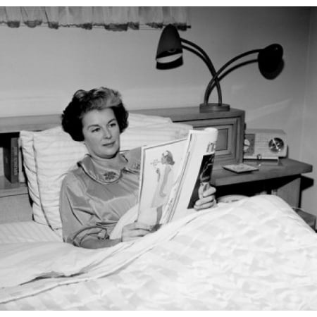 - Mature woman sitting in bed reading magazine Poster Print