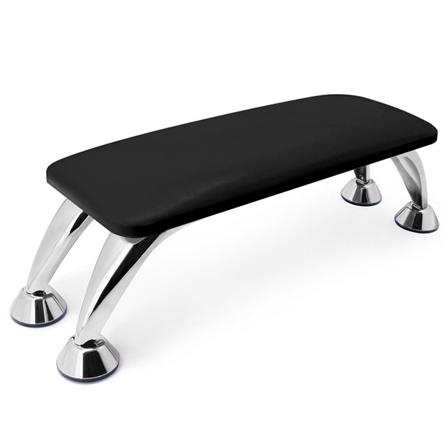 reposabrazos para uñas - reposabrazos de microfibra negro con diseño europeo; vista 3/4 frontal de superficie acolchada rectangular con esquinas redondeadas y cuatro patas arqueadas cromadas de acero inoxidable con bases antideslizantes, compatible con lámparas UV y fácil de limpiar; a menudo se usa también para apoyar herramientas durante manicuras profesionales.