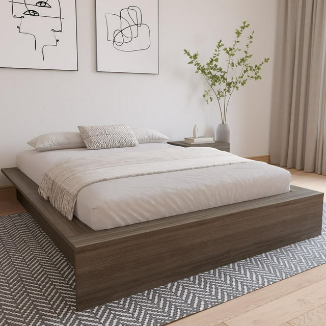 Nexera James Platform Bed featuring a sleek wood finish, dressed with light beige linens and decorative pillows, set on a patterned rug in a bright room with abstract wall art and greenery.