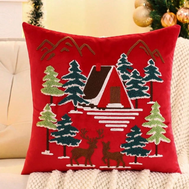 juego de cojines navideños de felpa con diseño de copo de nieve, árbol de navidad y lana bordada para sala de estar o sofá. Funda de cojín roja de 45x45 cm (17.7x17.7 in) vista frontal, felpa suave con bordado en lana de una cabaña nevada entre pinos y dos ciervos, puntadas y cremallera visibles; colocada sobre sofá con manta y decoración navideña al fondo, adecuada también como cojín decorativo para reuniones festivas.