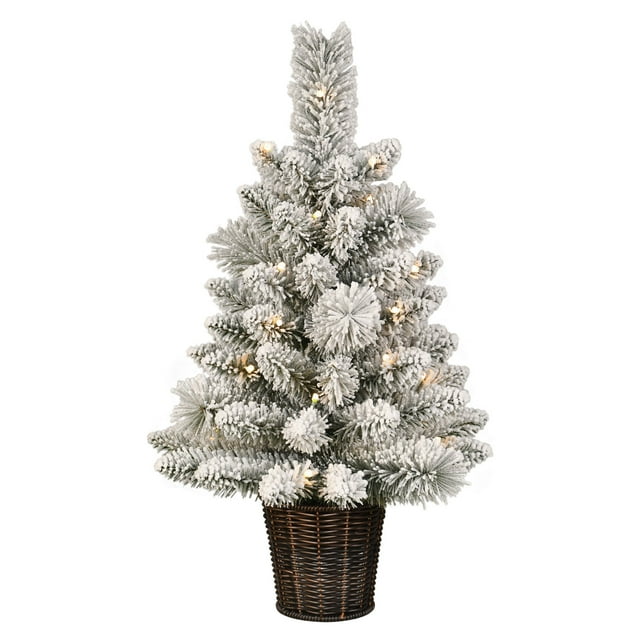 2-foot pre-lit green Christmas tree with white flocked branches and warm LED lights in a dark woven basket.