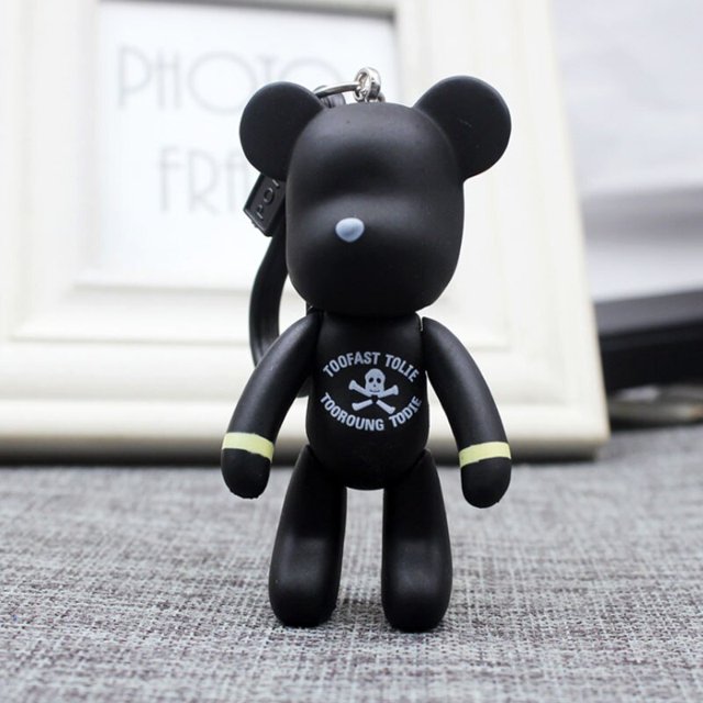 cuerda tejida de cuero bomgom popobe gloomy rhinestone llavero borla gafas oso llavero anillo titular bolso encanto colgante negro xuanjing unisex Llave colgante en forma de oso negro, vista frontal centrada; figura con nariz gris claro, impresión blanca de calavera y texto en el pecho, cuerda tejida unida a un anillo metálico (oro champán y plata según especificación); fondo interior neutro; accesorio de moda unisex y llavero de oso adecuado como adorno para llaves o bolso.