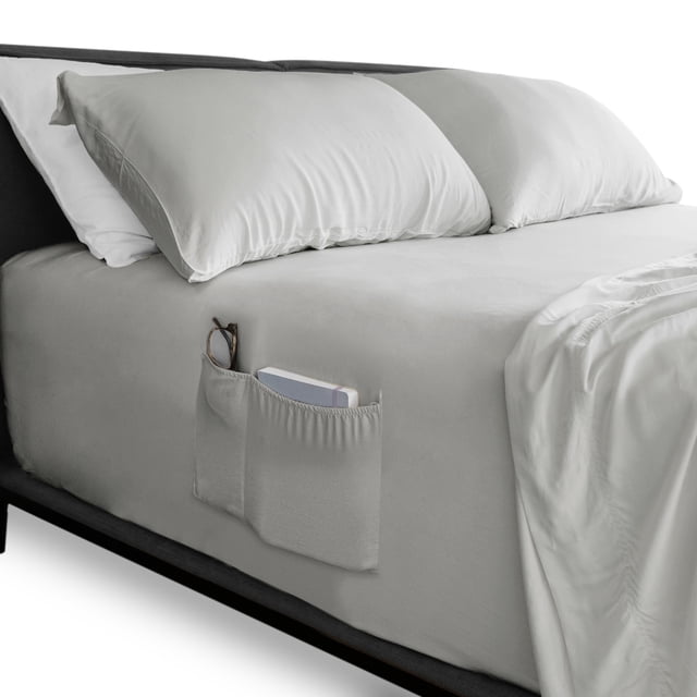 sábana de cajón queen size almaya inteligente ajuste perfecto mod gris, vista 3/4 en cama queen, sábana ajustable gris con bolsillo doble lateral que contiene lentes y un libro, cuatro bandas elásticas visibles para sujeción y tejido de alta suavidad y resistencia; suele usarse para guardar accesorios pequeños junto a la cama.