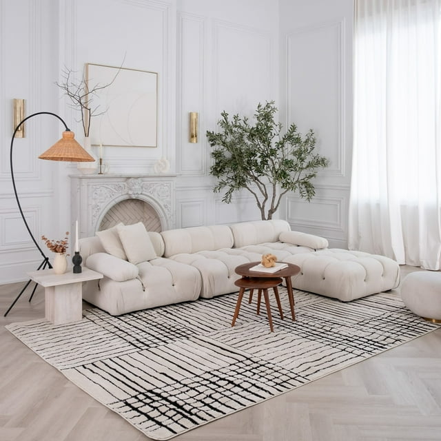 Cream and black abstract indoor area rug under a tufted cream sectional sofa in a modern living room with white walls and natural light.