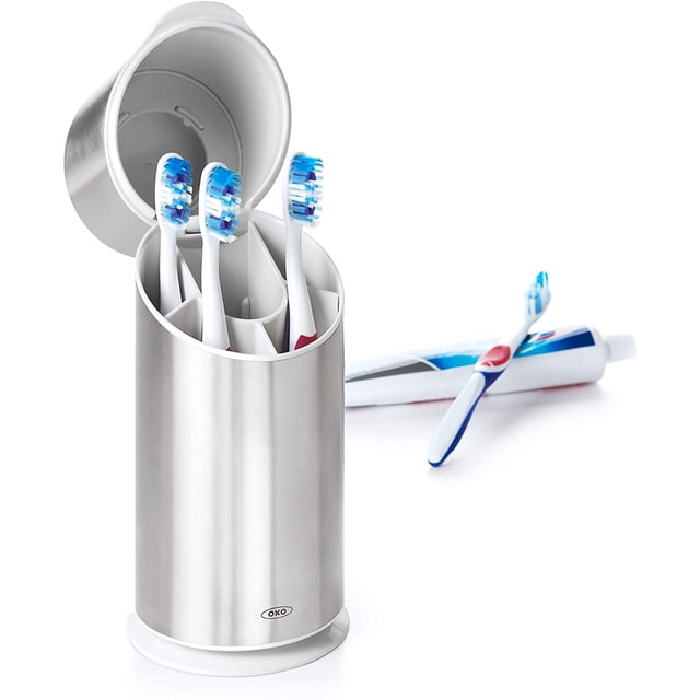 organizador para cepillos acero OXO con tapa abatible en vista frontal 3/4; cuerpo cilíndrico de acero cepillado con divisor extraíble y ranuras superior e inferior para ventilación, acomoda hasta 4 cepillos y un tubo de pasta, apto como organizador de baño.