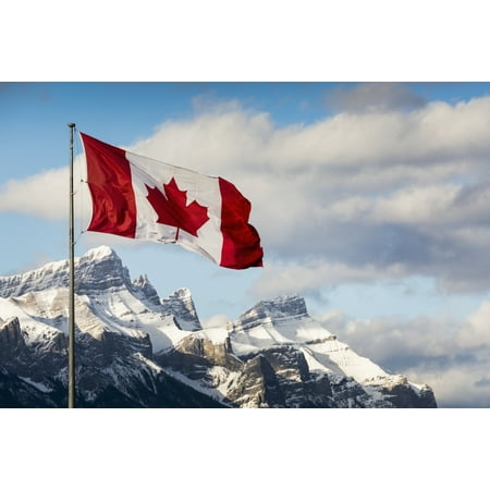 Canadian flag blowing in the wind on a flag pole with snow covered mountain range in the background with blue sky and clouds Canmore Alberta Canada Stretched Canvas - Michael Interisano  Design