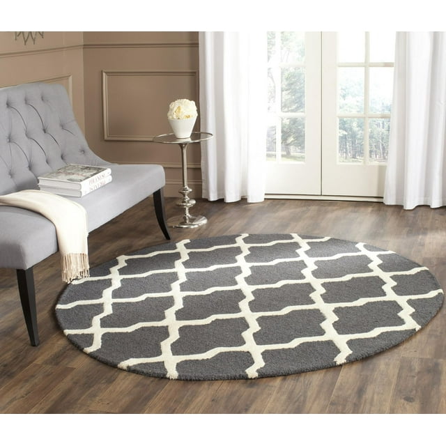 Safavieh Cambridge Liam round gray area rug featuring a white geometric lattice design placed on wood flooring next to a light gray tufted bench and silver side table.